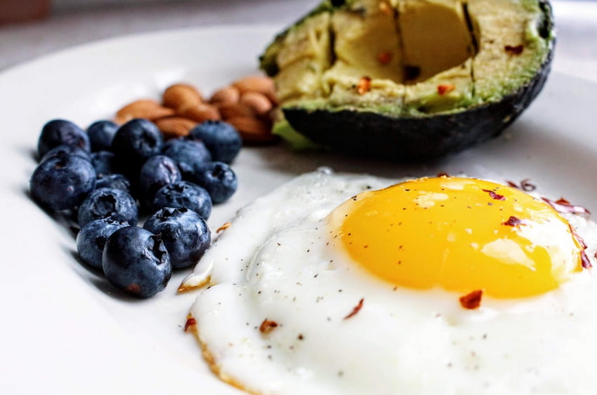 A plate featuring an avocado, fresh blueberries, and a cooked egg arranged together.  