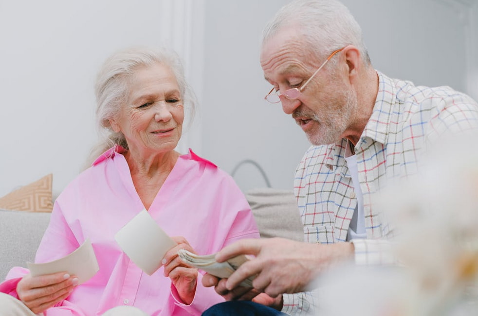 An older couple sits on a couch, examining a piece of paper together with focused expressions.  