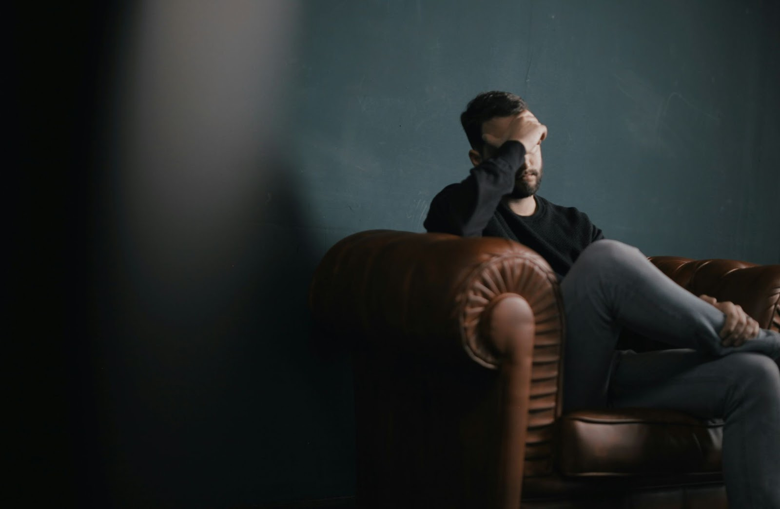 A man sits on a leather chair, resting his head in his hands, conveying a sense of stress or contemplation.  