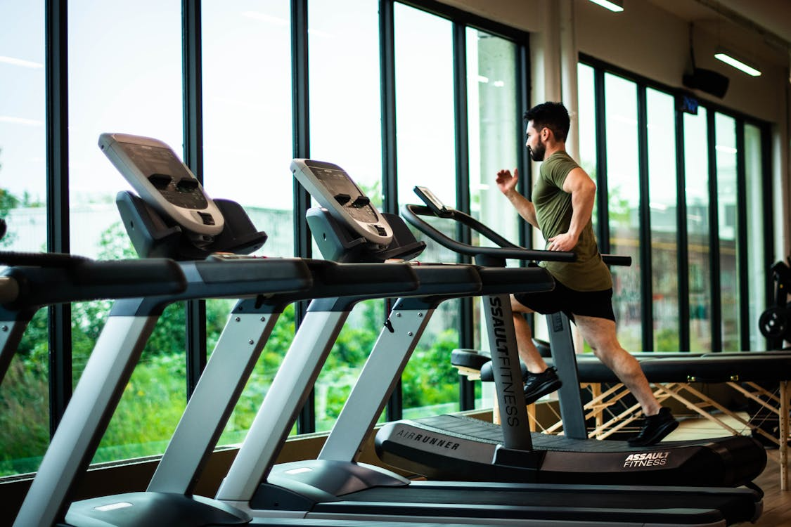 A man is jogging on a treadmill in a modern gym, focused on his workout amidst various gym equipment.  