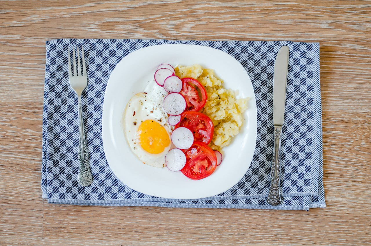 A plate featuring a fried egg, sliced tomato, radish, and onion arranged artfully.