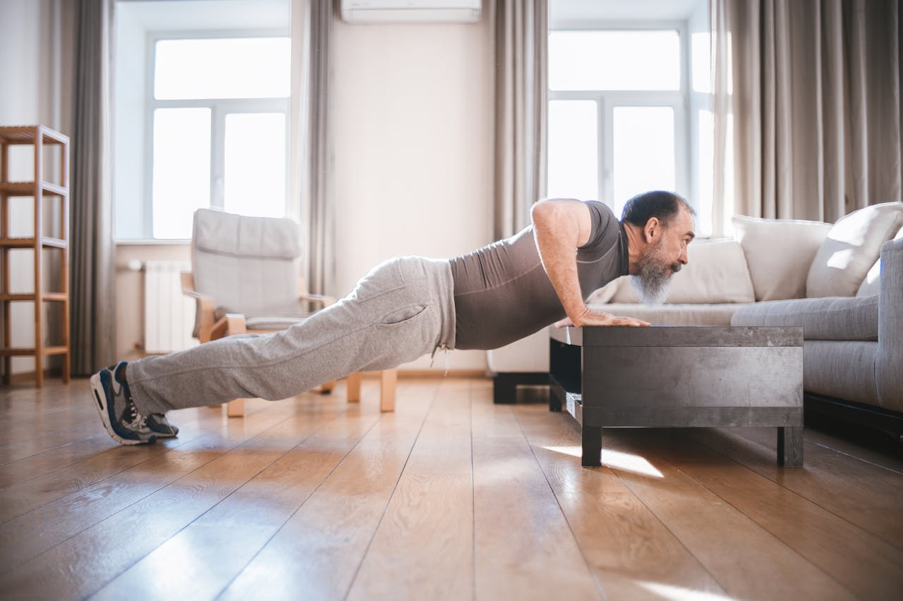 Man performing push-ups on a carpeted living room floor, surrounded by furniture and natural light from a window.