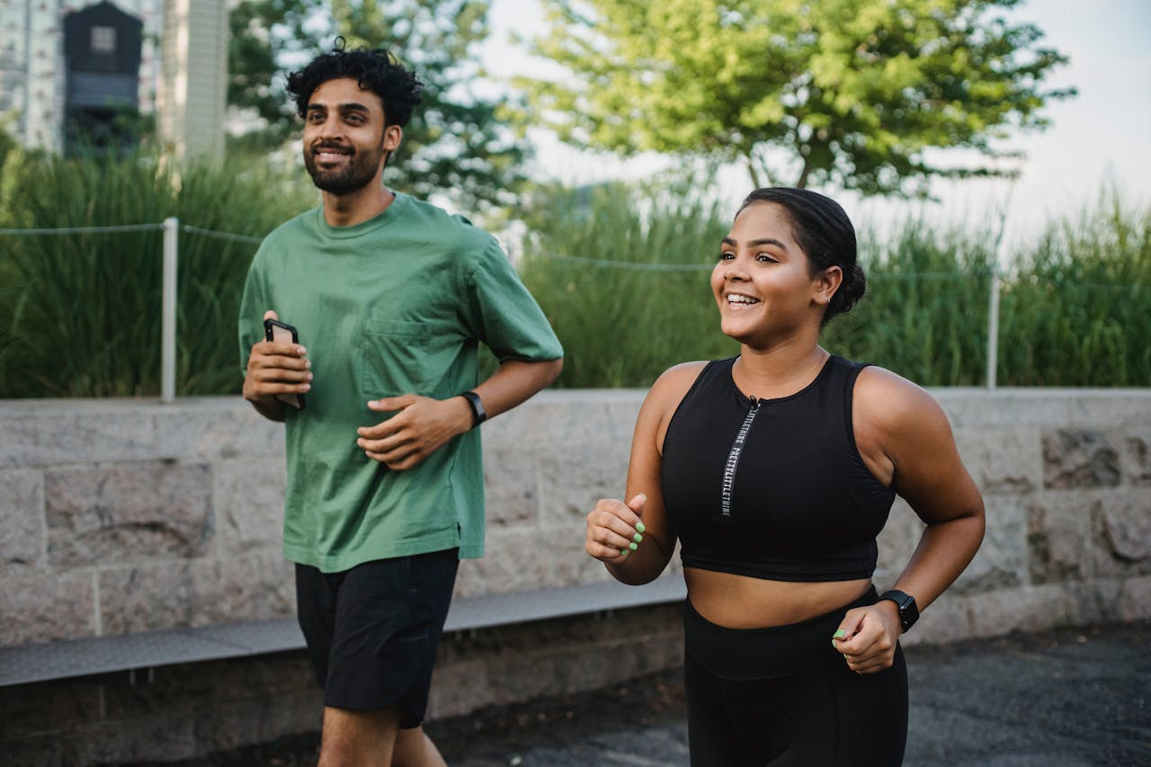 A man and woman jogging side by side on a sunny path, both wearing athletic clothing and smiling.  