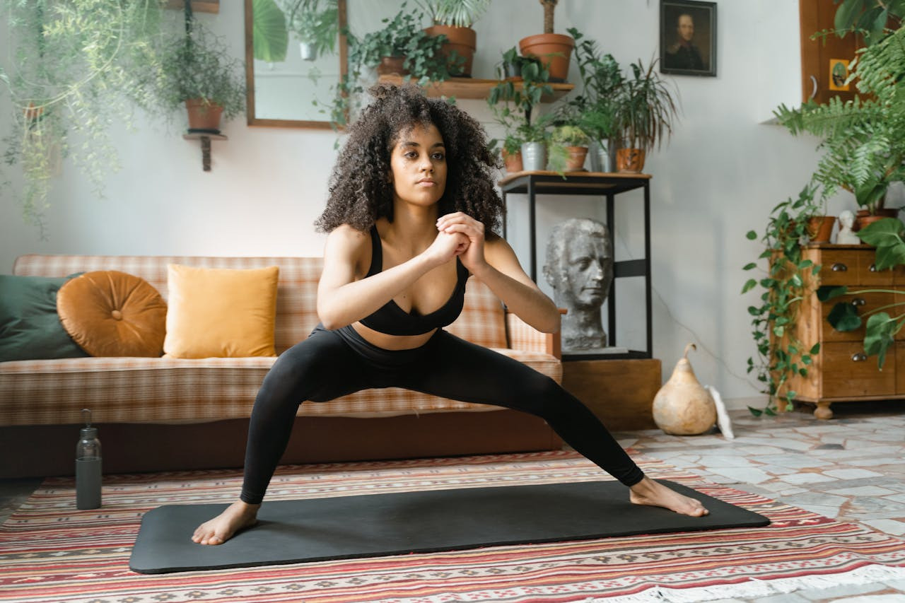 A woman in a black sports bra and leggings practices yoga on a mat, demonstrating a focused pose in a serene environment.