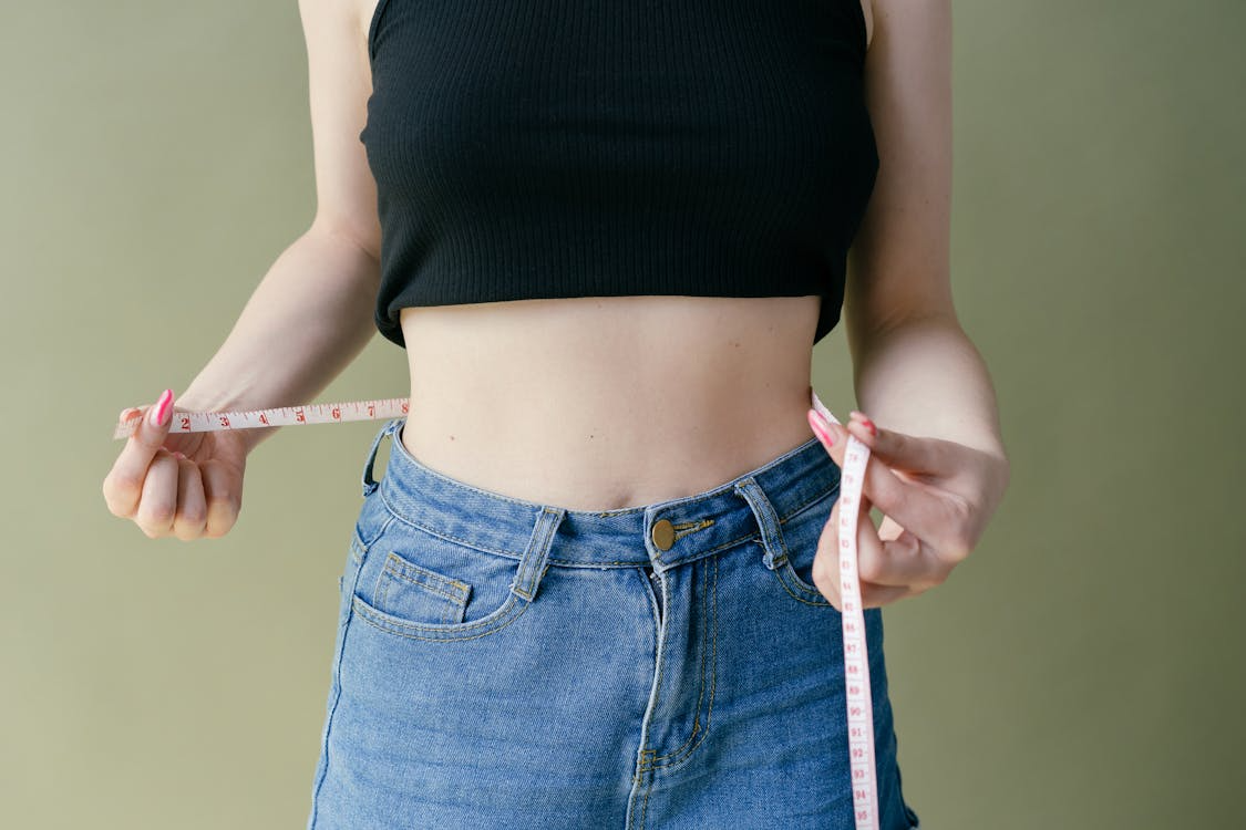 woman wrapping a measuring tape around her waist to track the progress of taking collagen to help lose weight