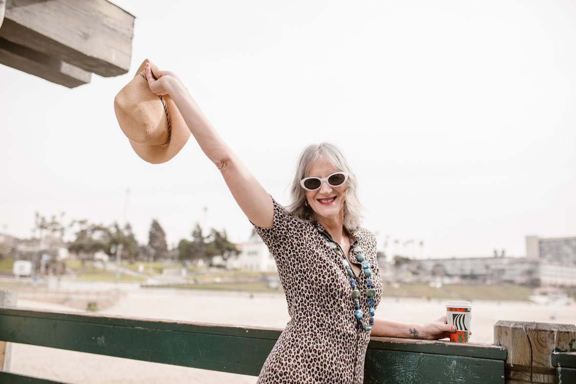woman with gray hair and fun sunglasses taking her hat off in a joyful travel photo