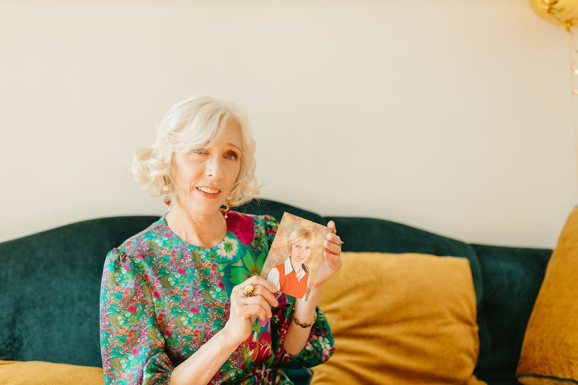 Older woman with great hair and skin posing with a photograph of her younger self