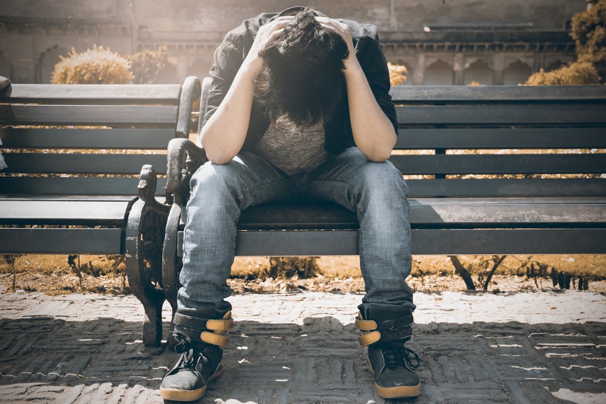 young man sitting on a park bench with his head in his hands