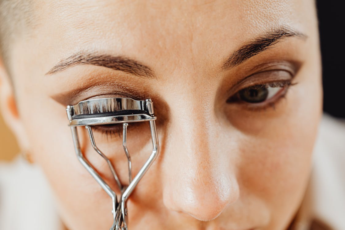 woman using an eyelash curler to improve the appearance of her lashes