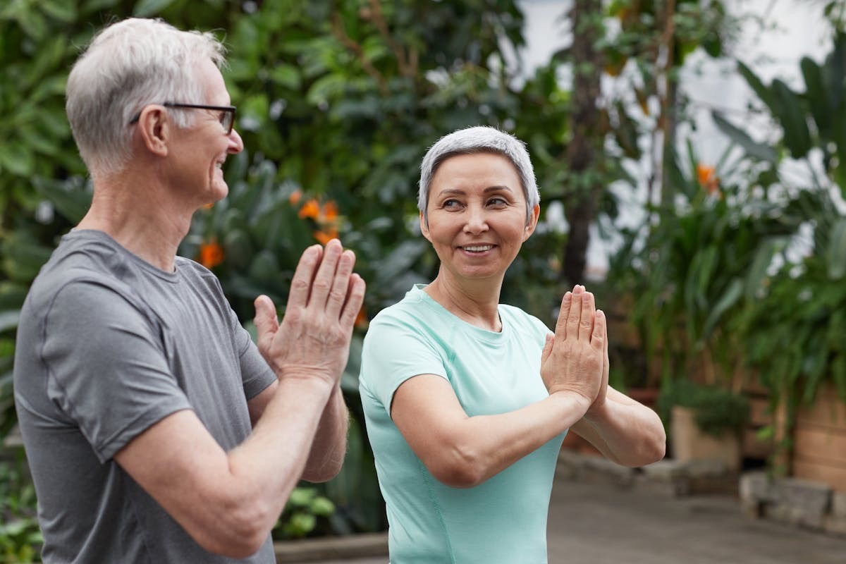 older couple with healthy muscle tone smiling at each other as the perform a yoga pose