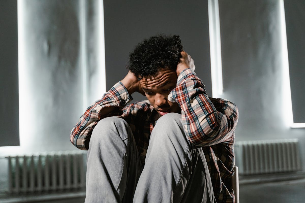 man dealing with chronic stress sitting on the floor, holding his ears