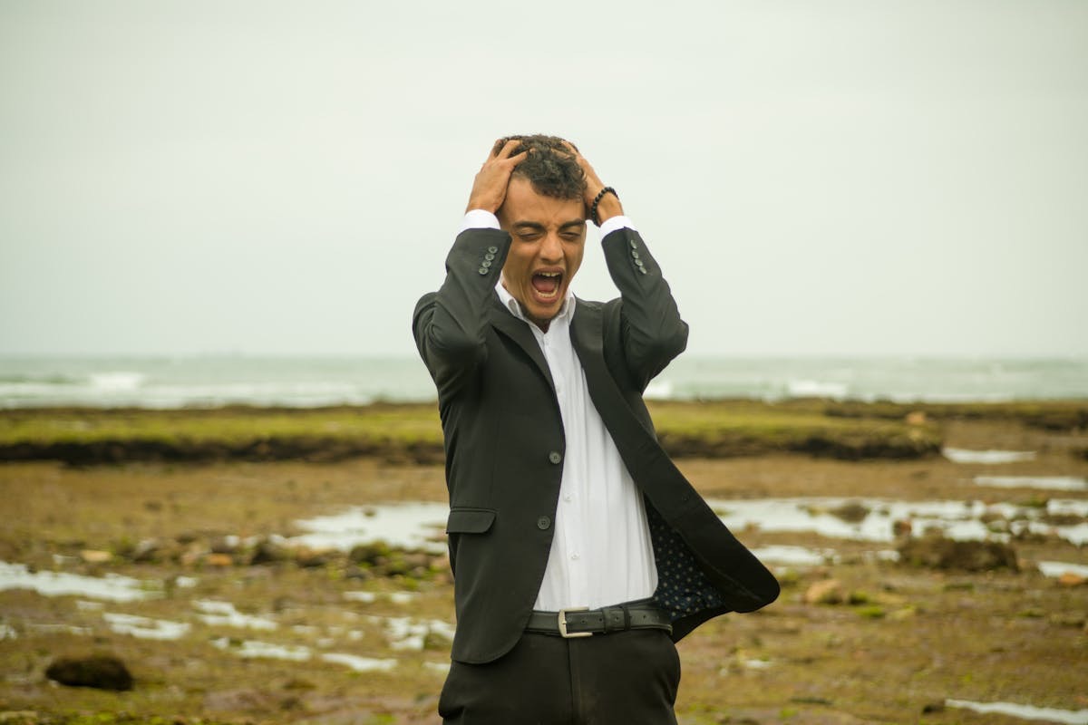 man in a suit holding his head and screaming by the see, anxious and alone