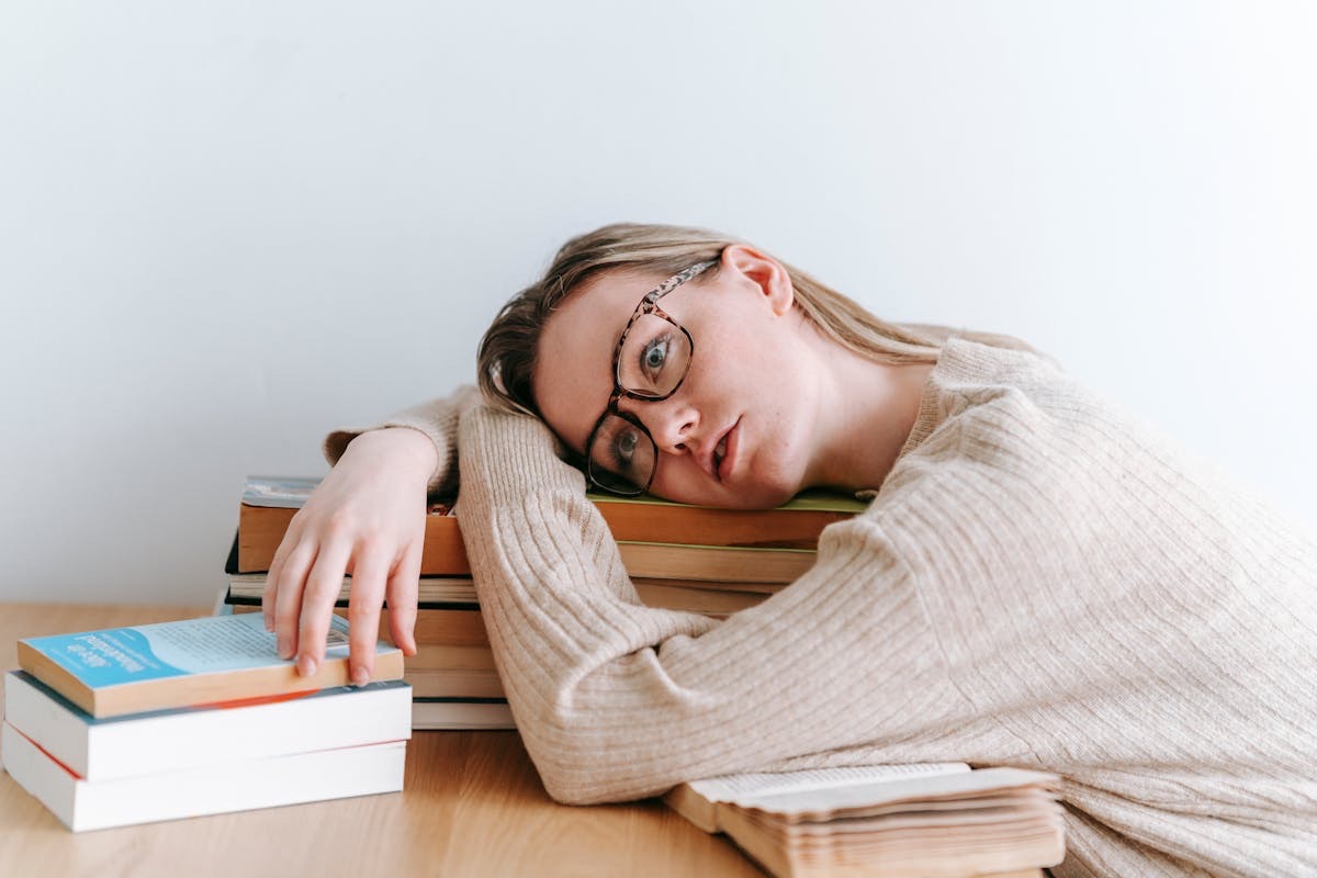 tired woman resting her head on a stack of books
