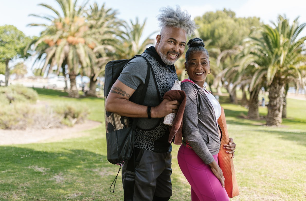 healthy older couple posing together in athleticwear on their way to an outdoor yoga class