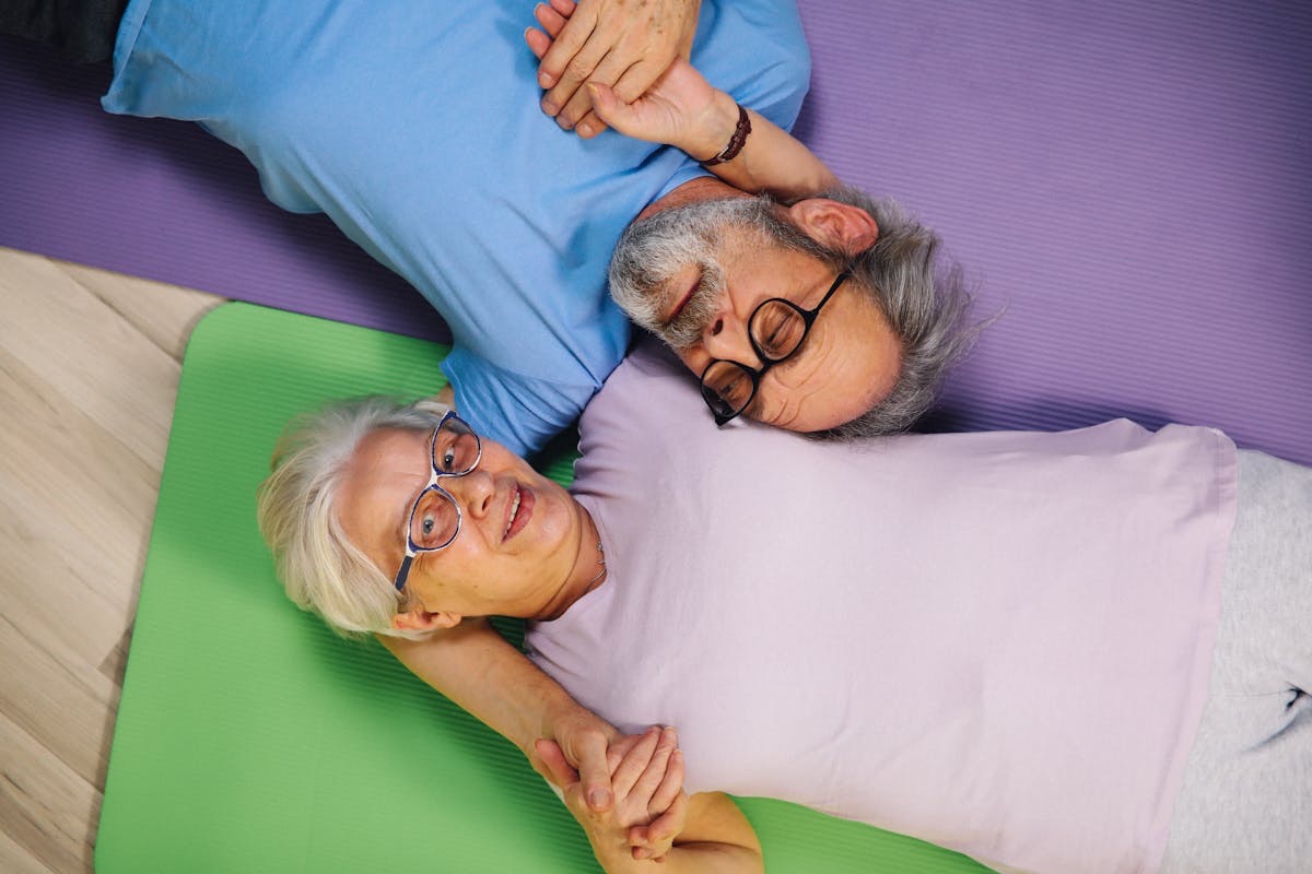 active older couple holding hands as they lie next to each other on their yoga mats
