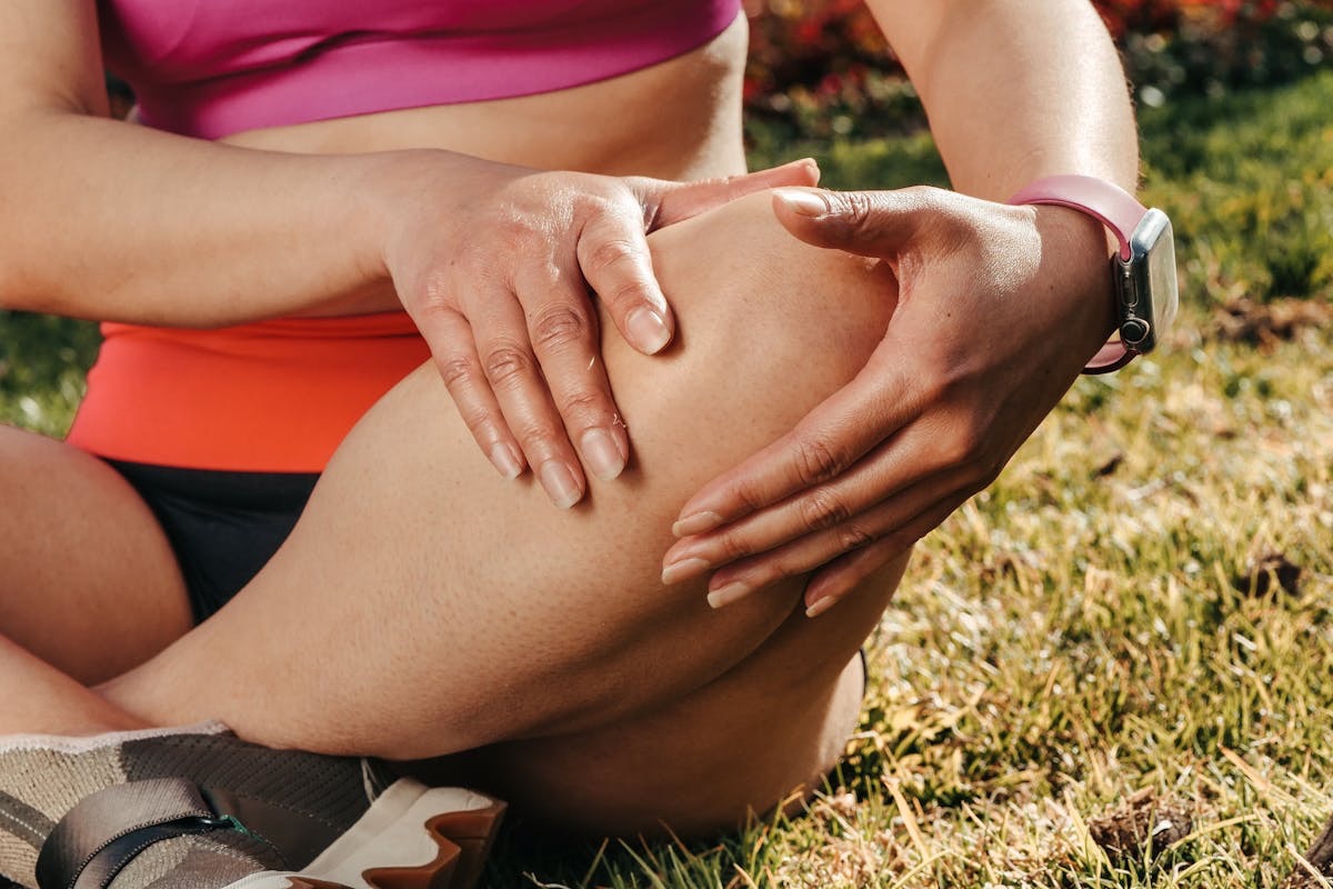 athlete suffering from knee pain holding their sore joint as they sit on the ground