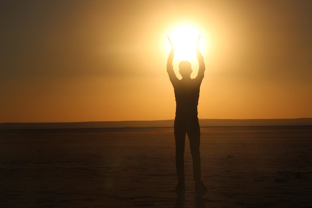 man silhouetted against a sunset so it looks like he's holding the sun over his head, a symbolic pose of light and optimism