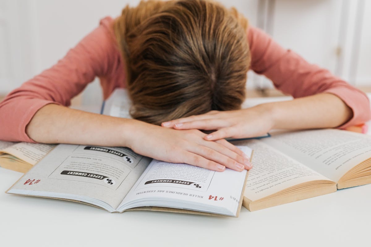 woman lying with her head on her open books due to fatigue