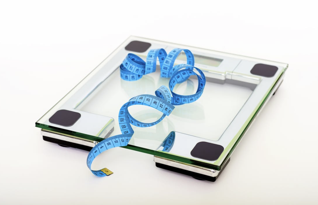 blue measuring tape curled on top of a scale representing weight loss