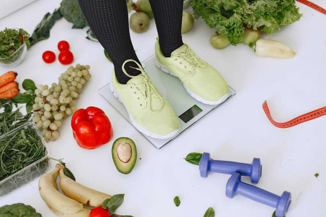 person standing on a scale surrounded by vegetables and fruits