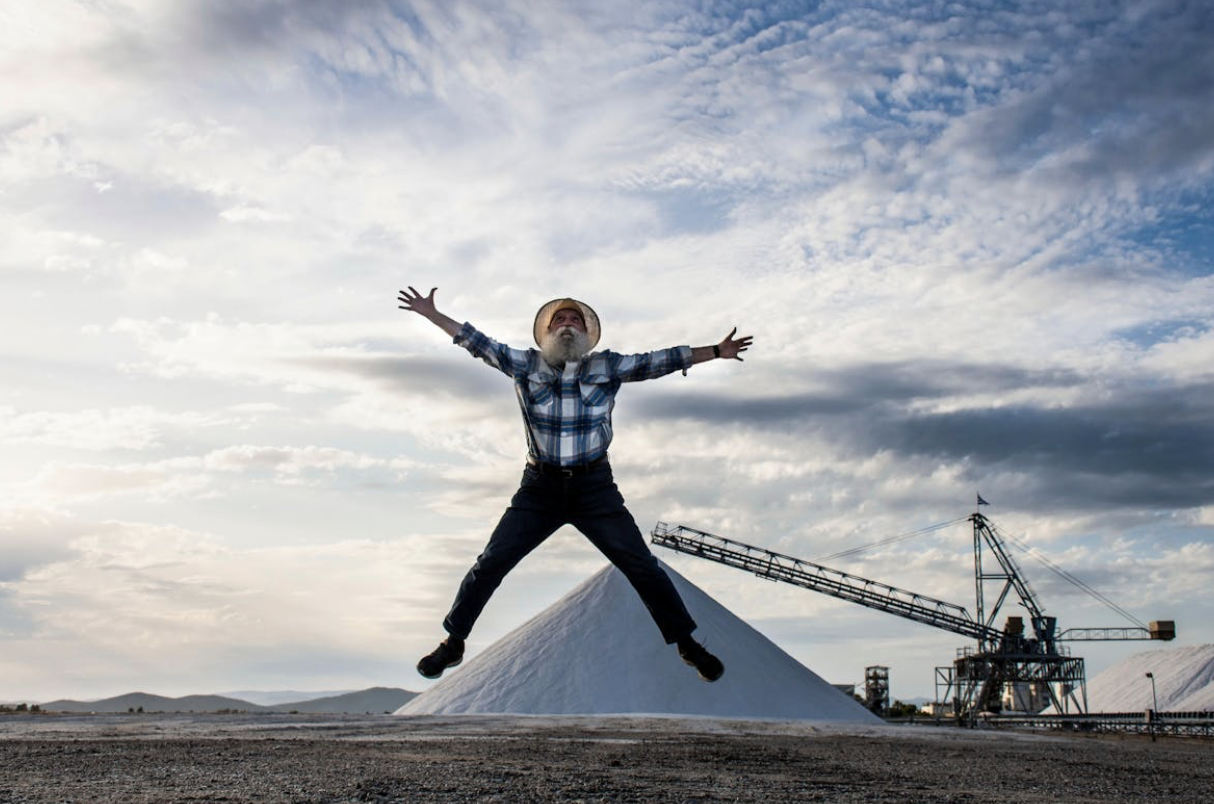 older man leaping in a star pose in front of a cheerful blue sky