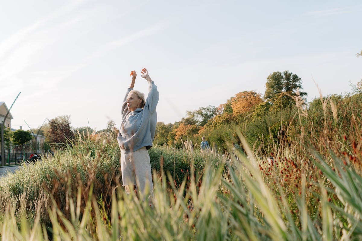 woman stretching as she walks through a field of tall grass