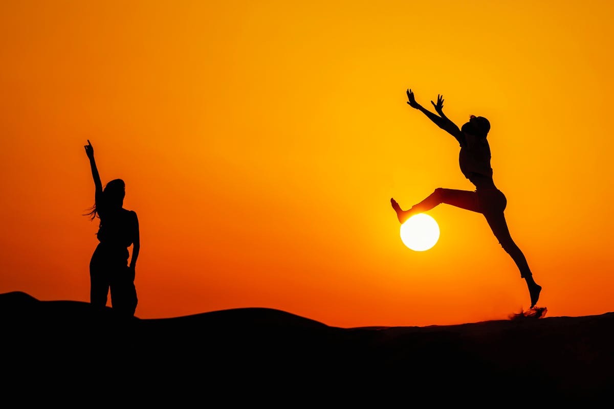 figures dancing silhouetted against a vibrant orange sky as the sun sinks toward the horizon
