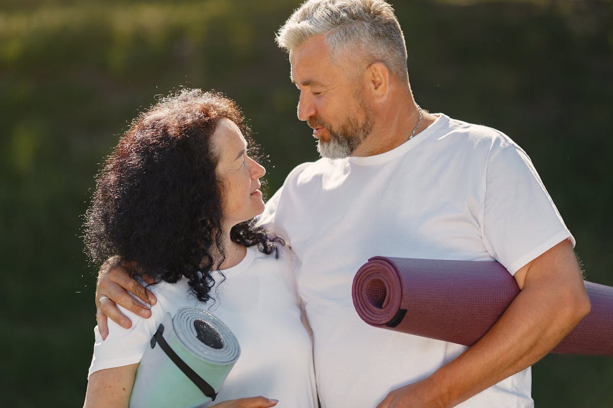 older couple with a yoga matts rolled under their arms gazing into each others eyes