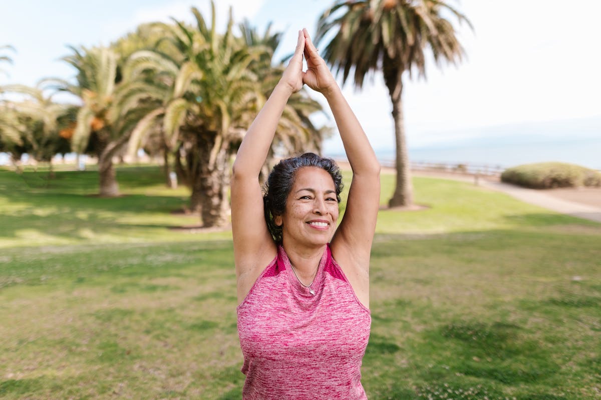 woman with graying hair doing yoga on a golf course with palm trees in the background