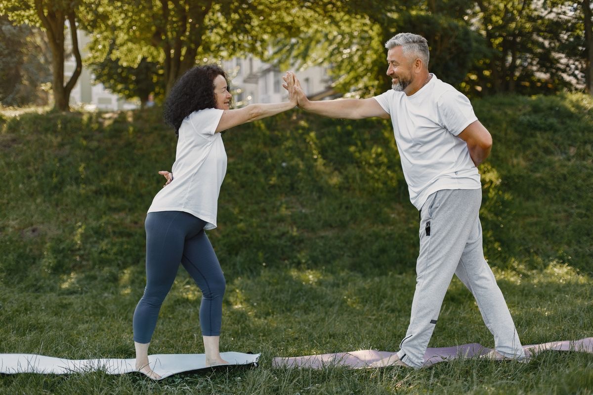 older couple high fiving while doing yoga outdoors