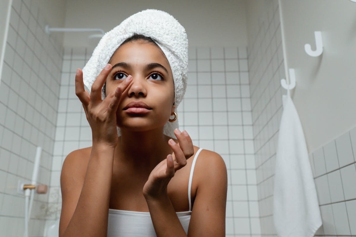 woman examining her skin in a mirror with her hair wrapped in a post-shower towel 