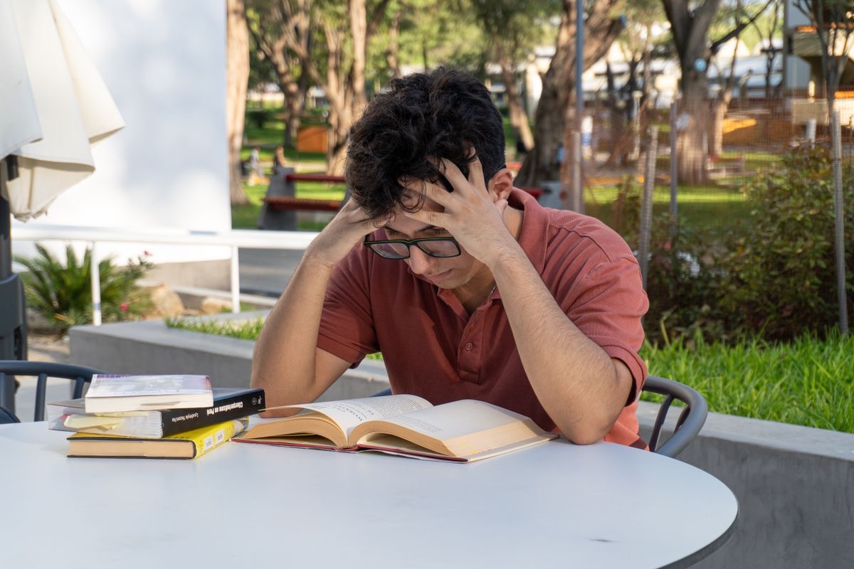 anxious man with books spread out on the table in front of him trying to study
