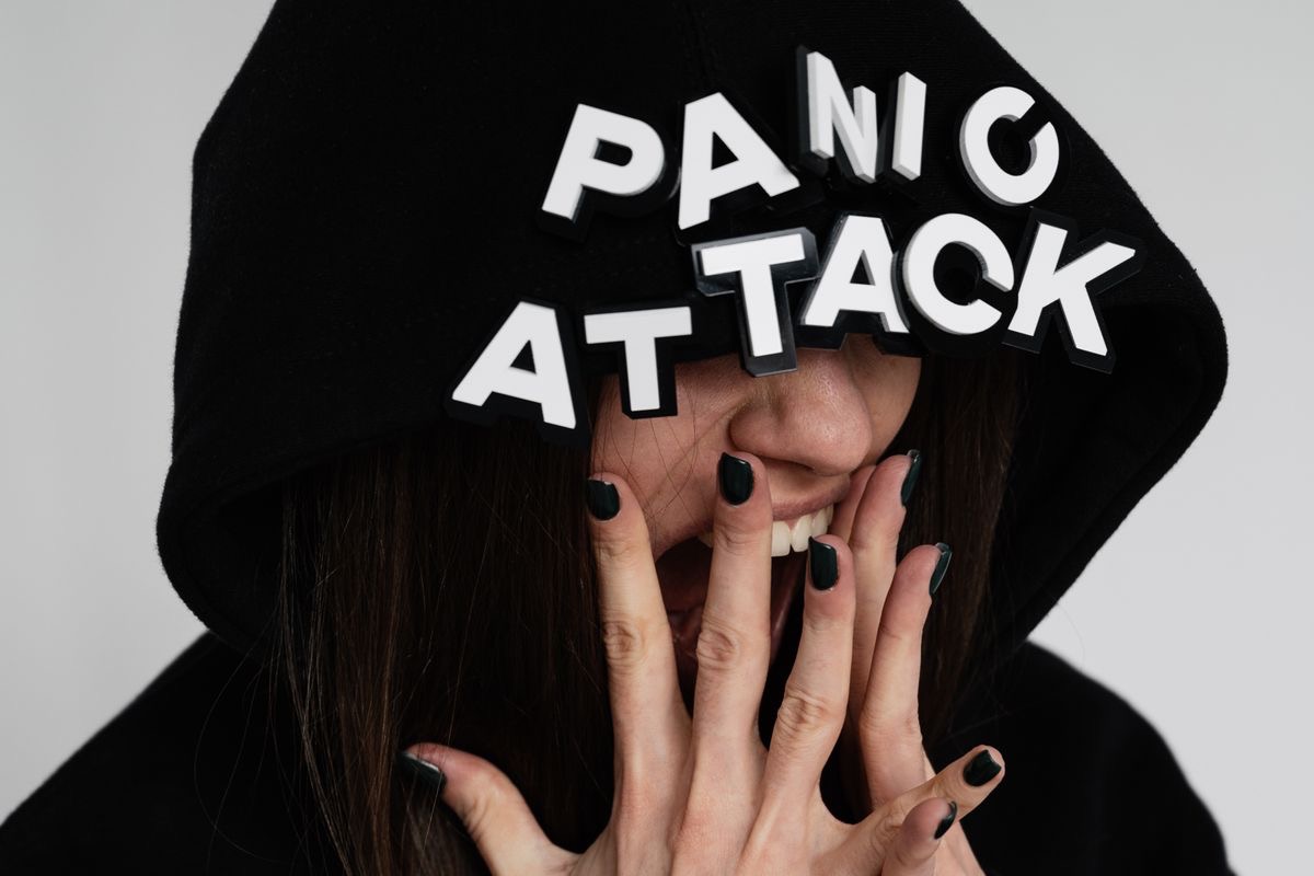stressed woman with a black hoodie pulled over her eyes with the words Panic Attack plastered across the hood