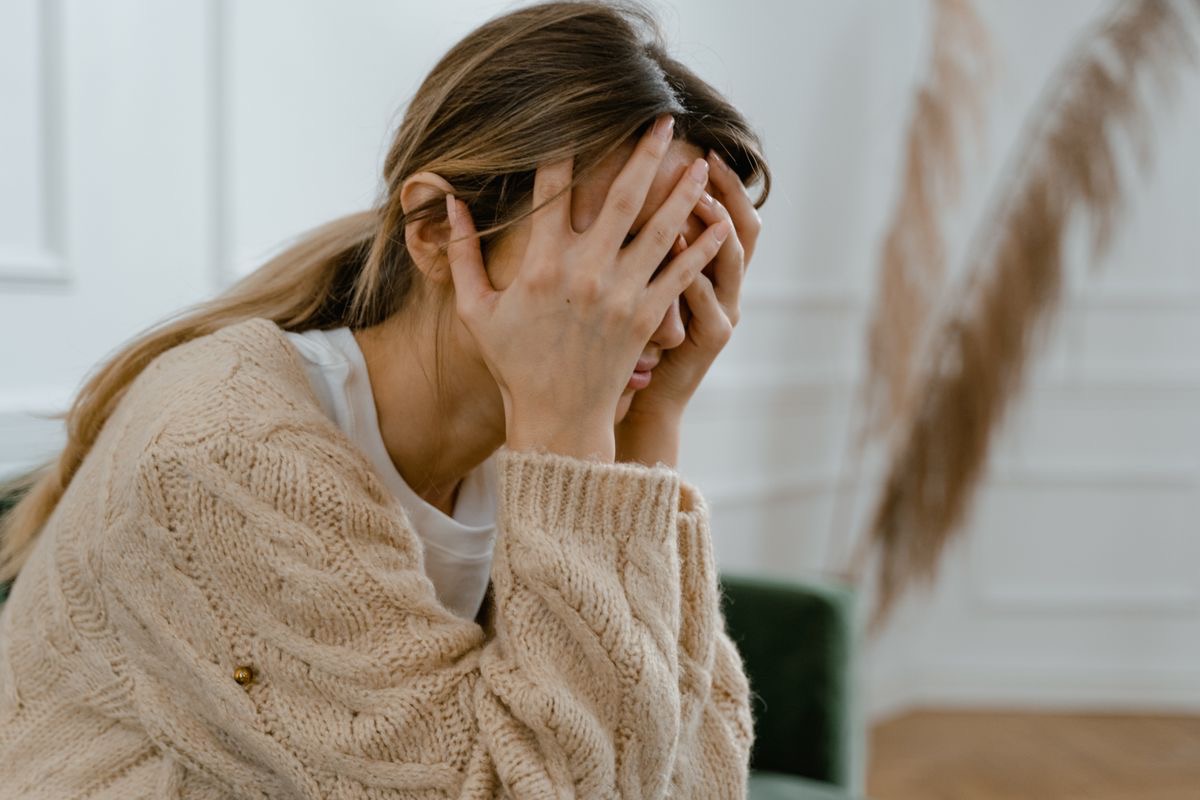 stressed woman in a beige sweater holding her head in her hands during a moment of anxiety
