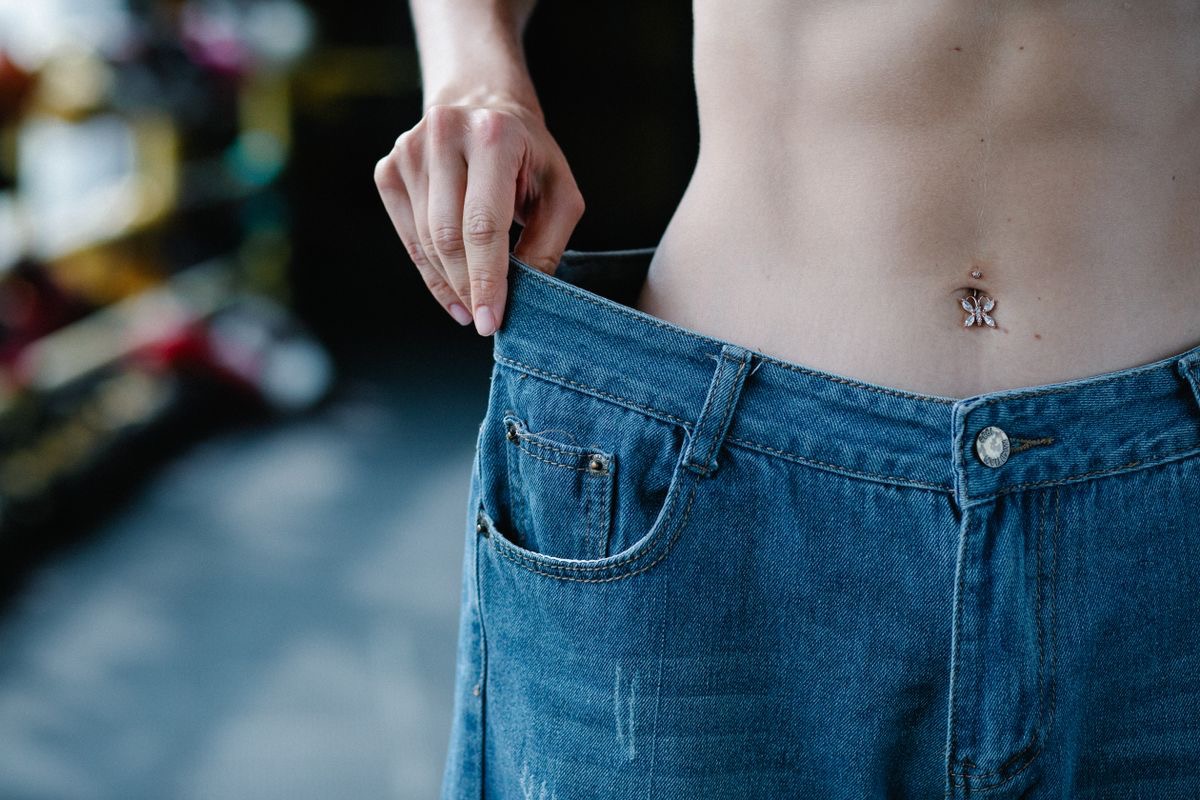 woman with a flat stomach showing off weight loss results by wearing her old pants, which are now far too big for her slim frame
