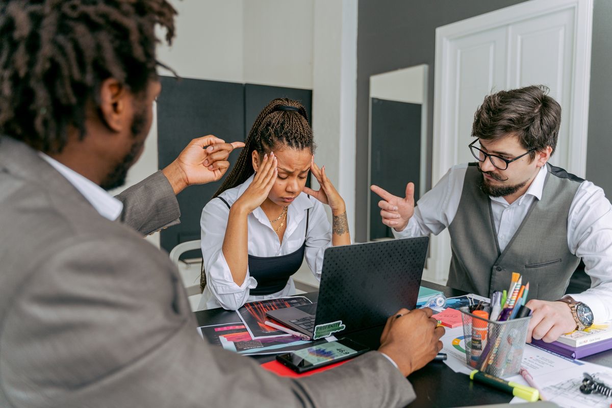 stressed woman sitting between two arguing men at work