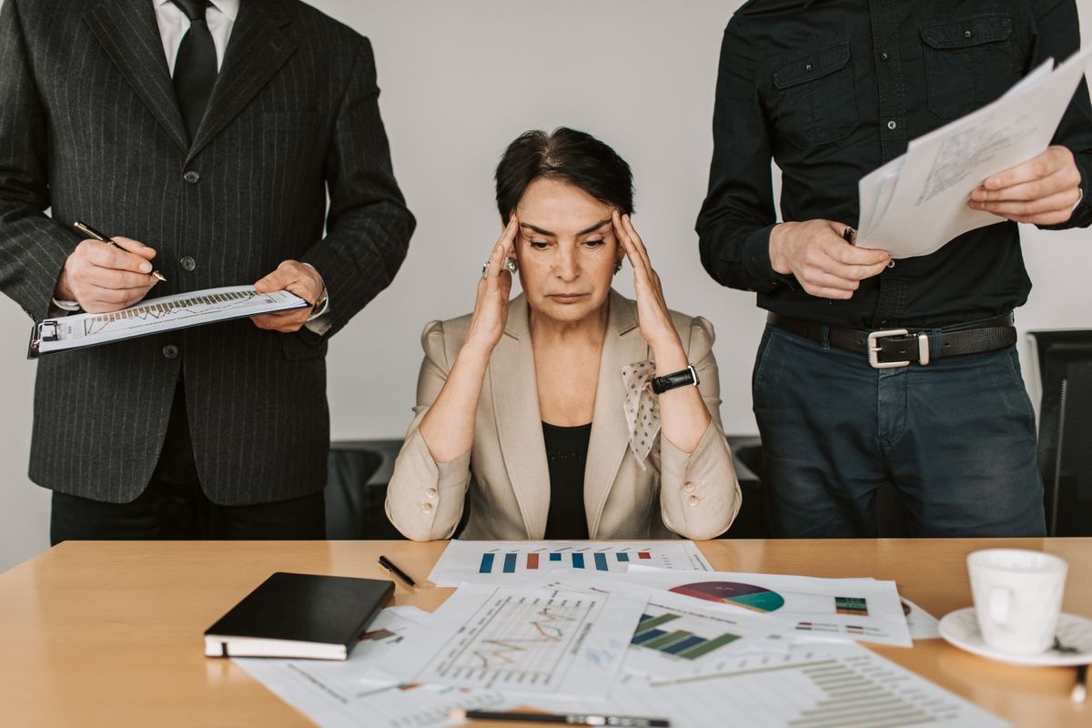 stressed boss woman surrounded by employees giving her reports