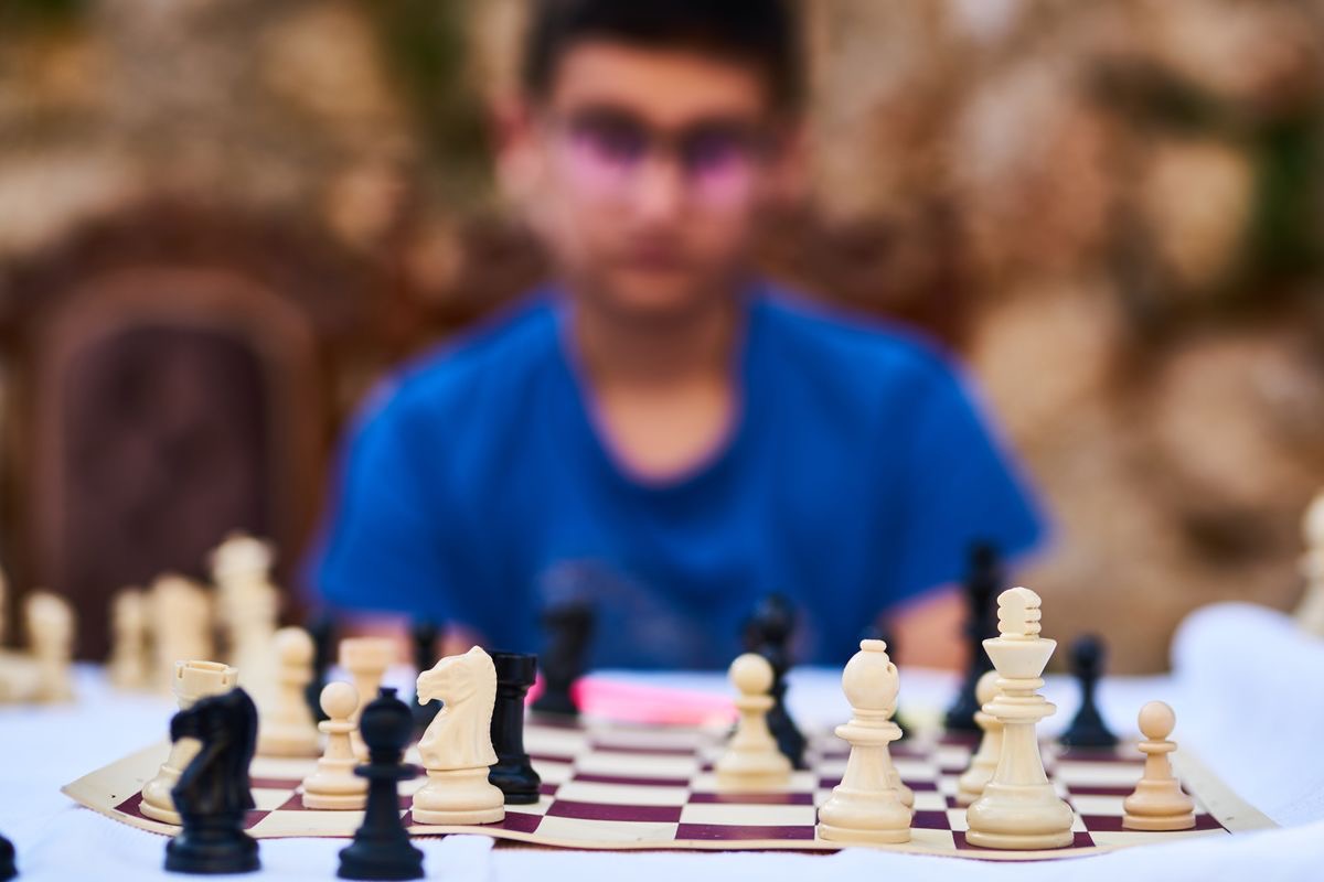 out of focus photo of a man sitting in front of a chess board with the board in focus in the foreground