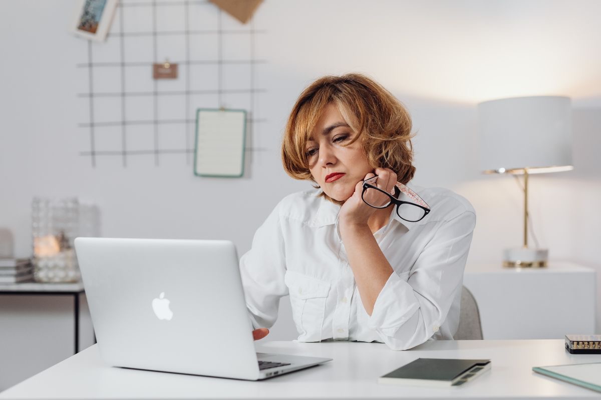 woman looking tired as she sits at her desk in front of a laptop