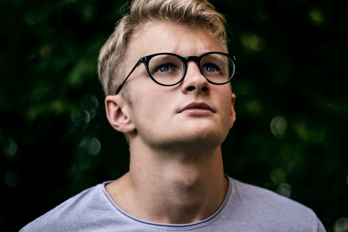 young man wearing glasses looking off into the distance, deep in thought