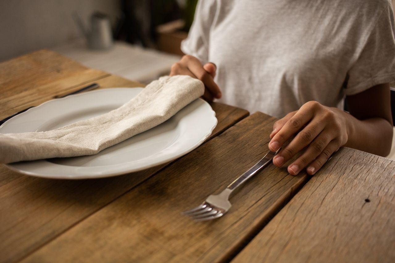 woman seated before a plate that's empty save for a folded napkin, representing intermittent fasting
