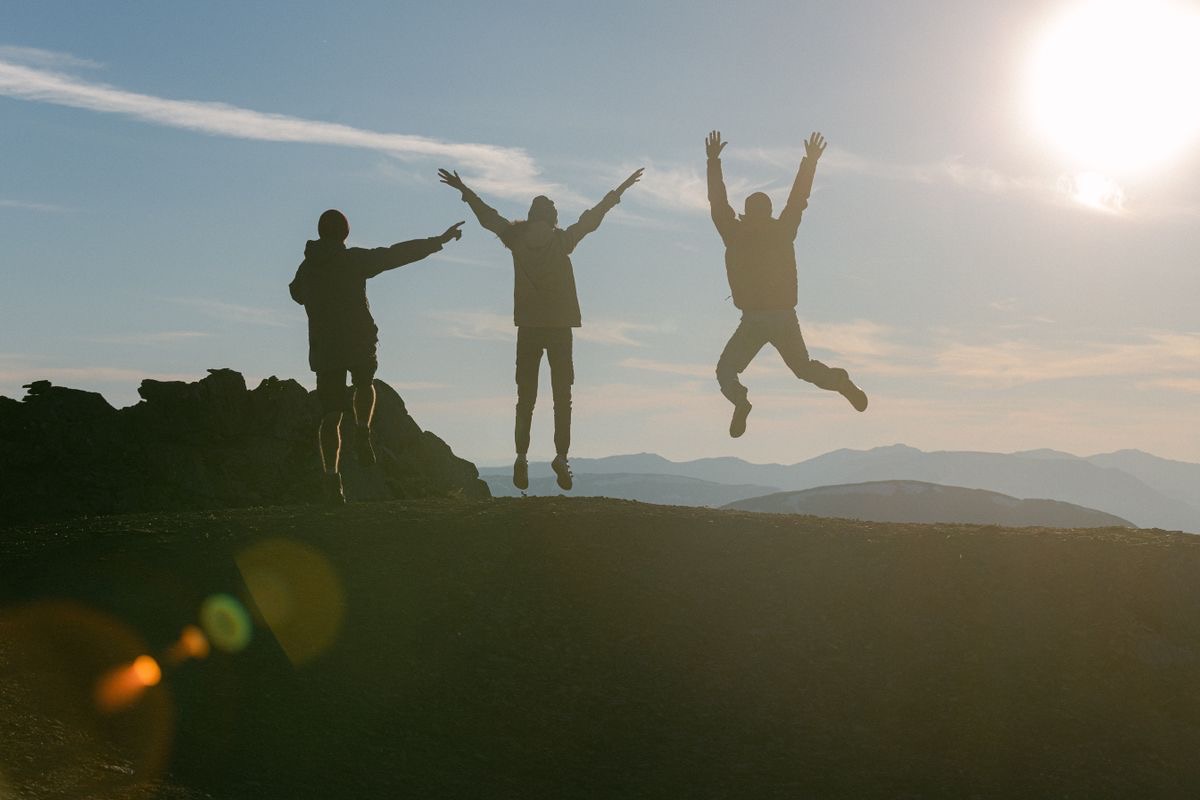 three energetic figures leaping backlit by the sun