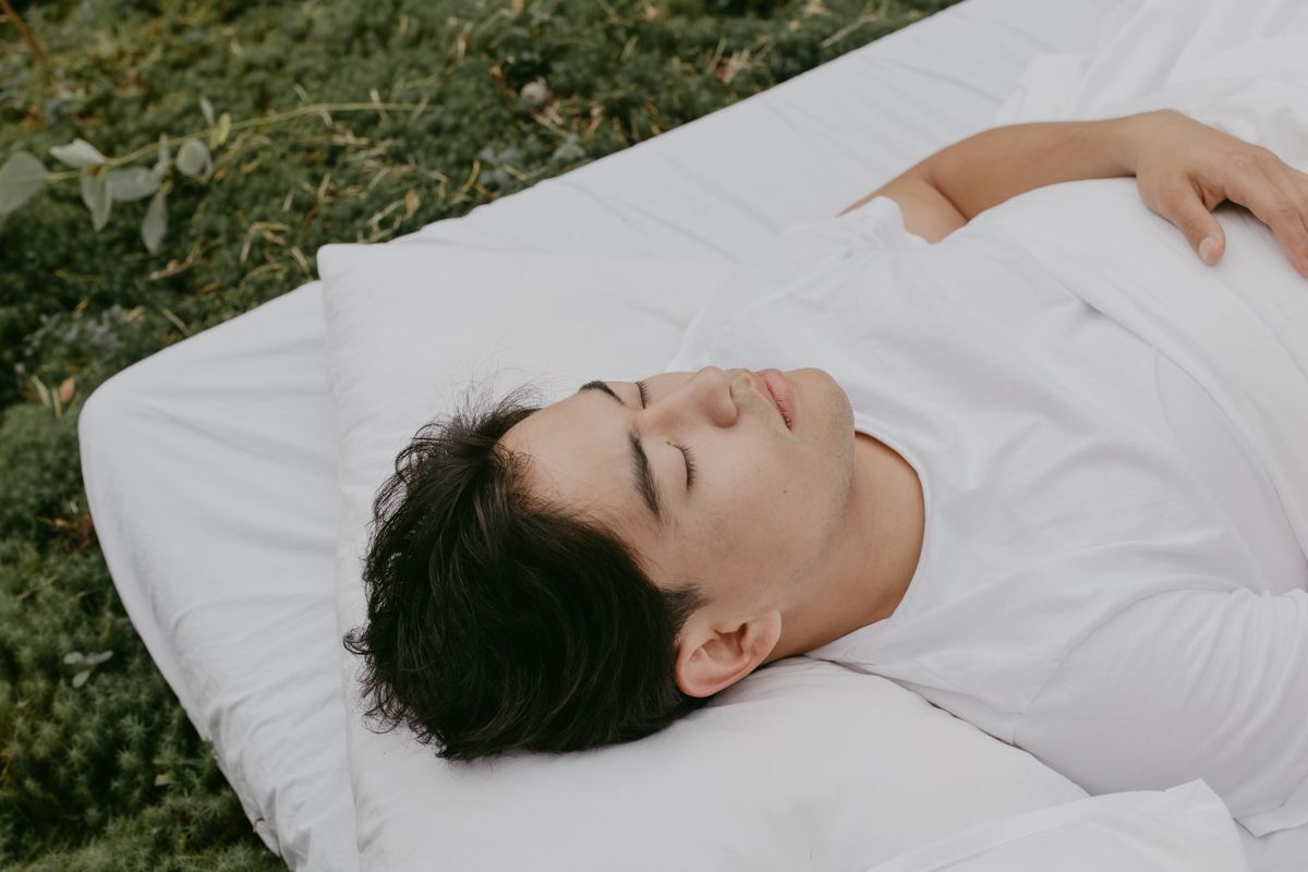 man lying on a white cot dozing outdoors