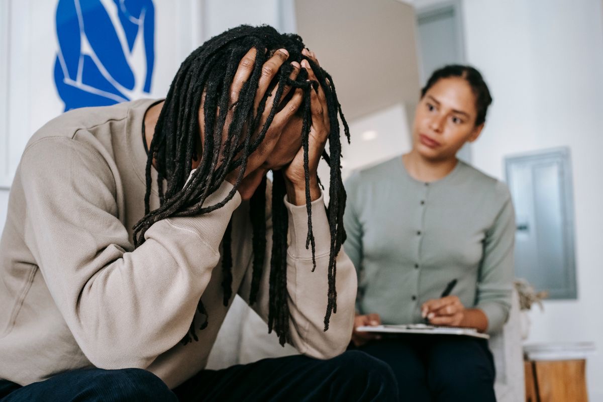 man with anxiety holds his head in his hands as a therapist offers guidance and support