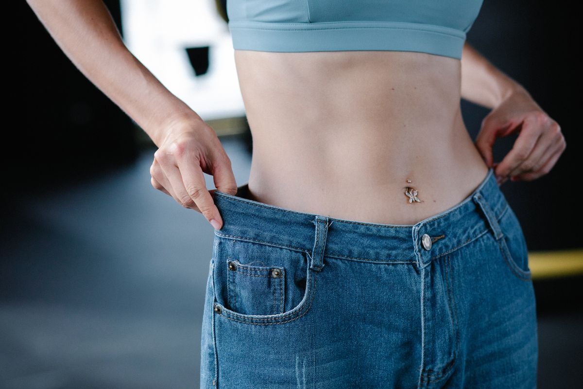 woman with a flat stomach wearing pants that are too large, showing how much weight she's lost as a result of natural glp-1 alternatives