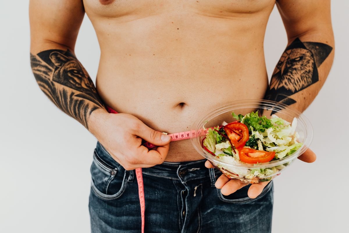 man with a measuring tape wrapped around his waist holding a nutrient dense salad