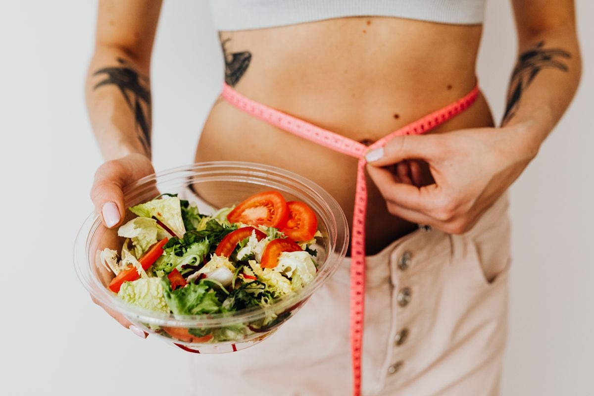 woman with a measuring tape wrapped around her waist holding a nutrient dense salad