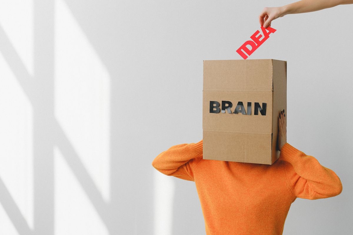 hand reaching out to place the word idea into a box labeled brain, which a stressed looking figure is wearing over their head