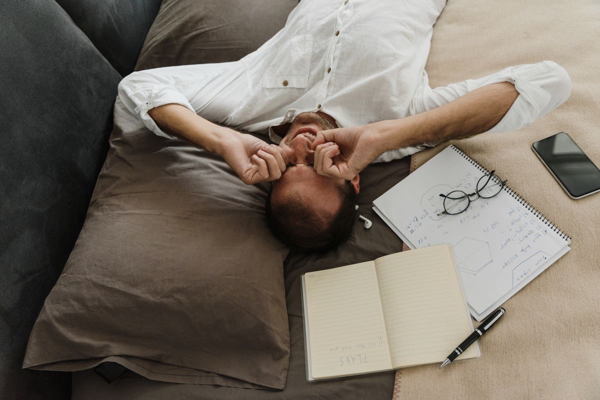 man with brain fog lying back looking frustrated while unfinished work papers scatter around him