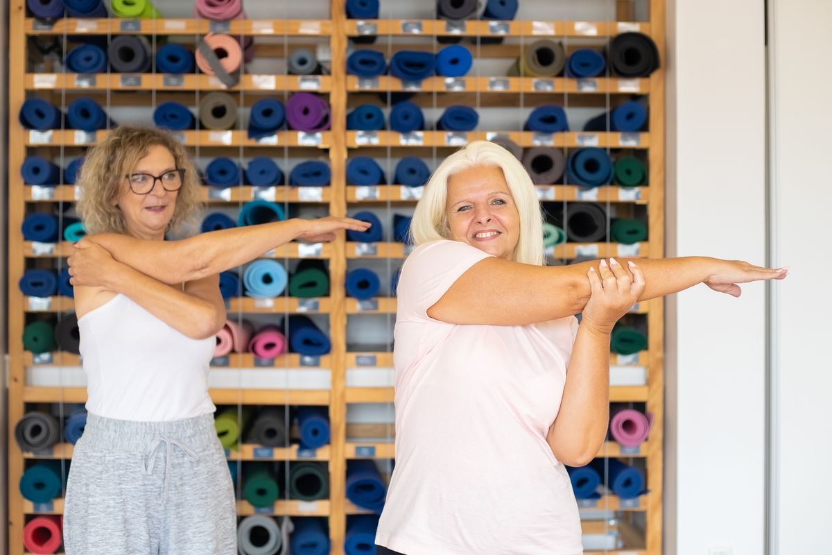 two older women stretching and chatting during yoga class